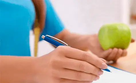 nutricionista com uma maçã verde na mão e escrevendo no papel com uma caneta.